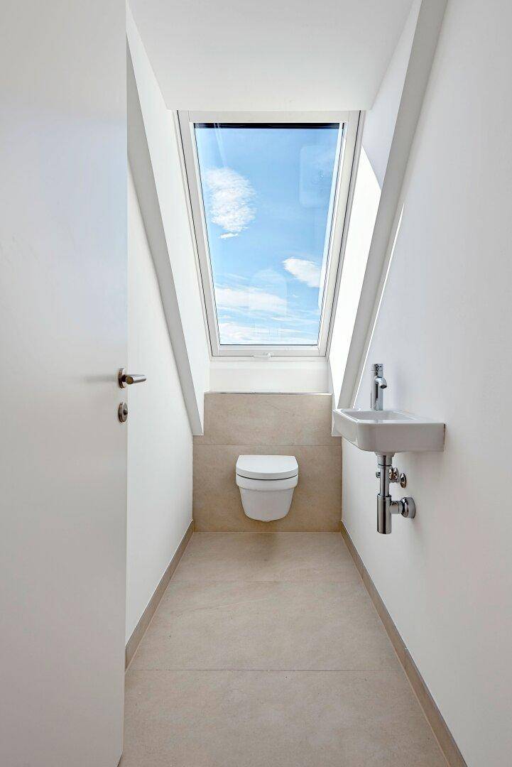 Modernes Gäste-WC mit wandhängender Toilette, kleinem Waschbecken und einem Dachfenster.
