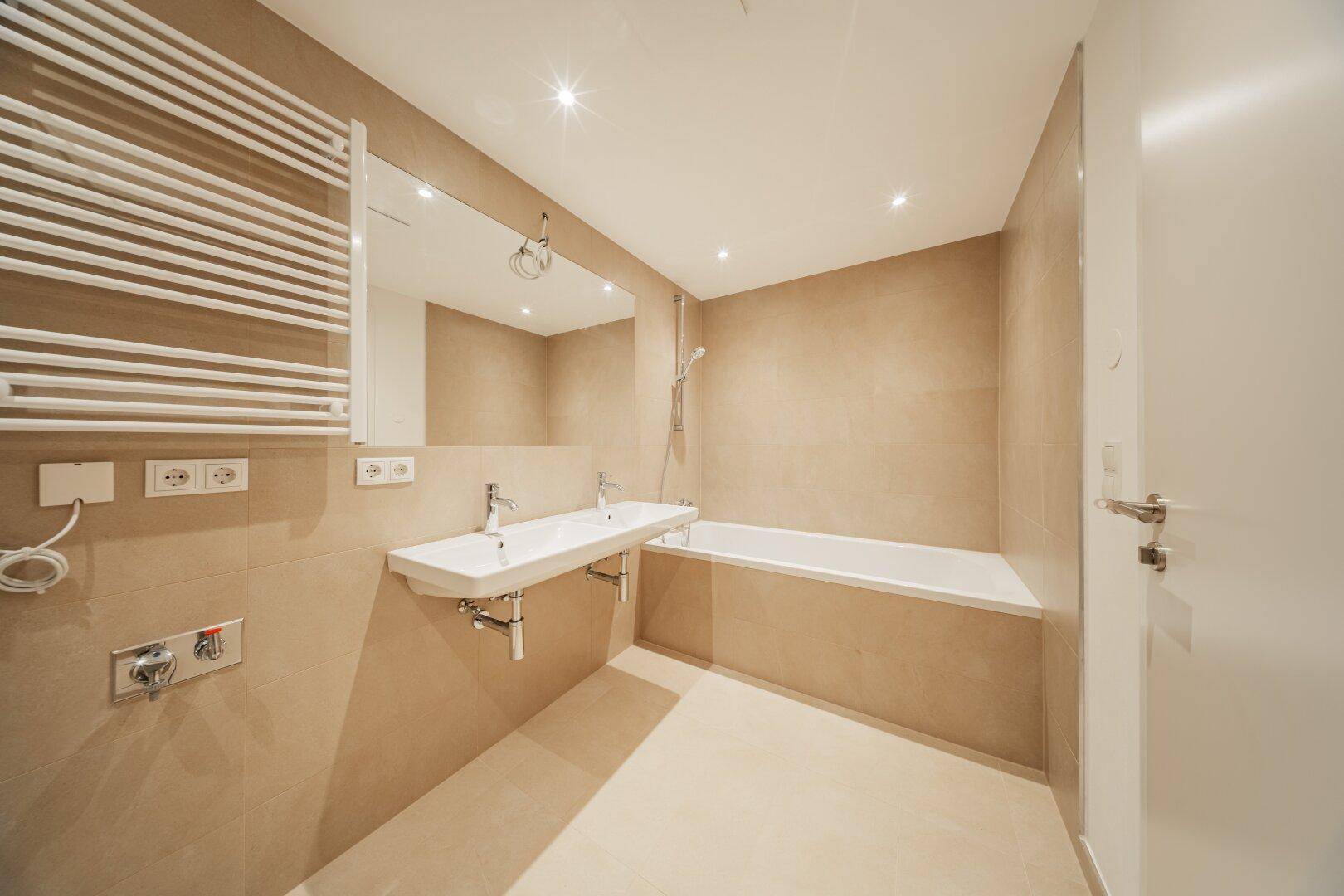 Modernes Badezimmer mit Doppelwaschbecken, Badewanne und beheiztem Handtuchhalter.