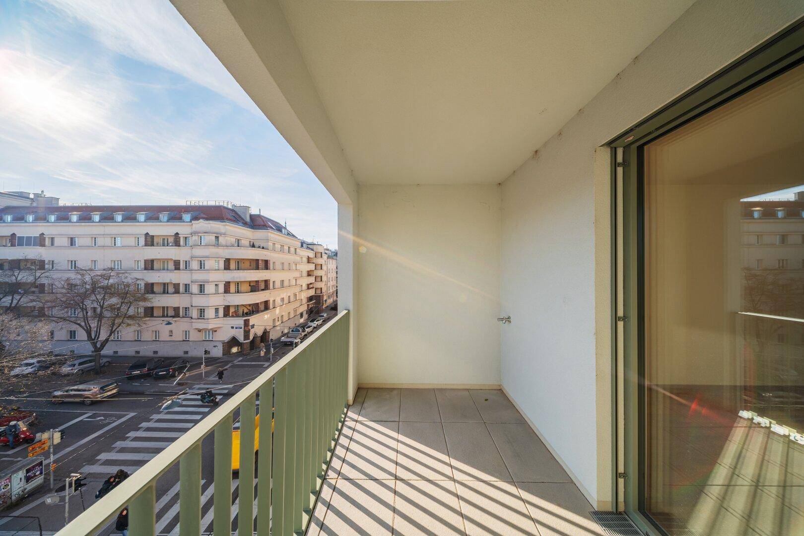 Balkon mit Fliesenboden und Blick auf die belebte Stadtstraße und historische Gebäude.