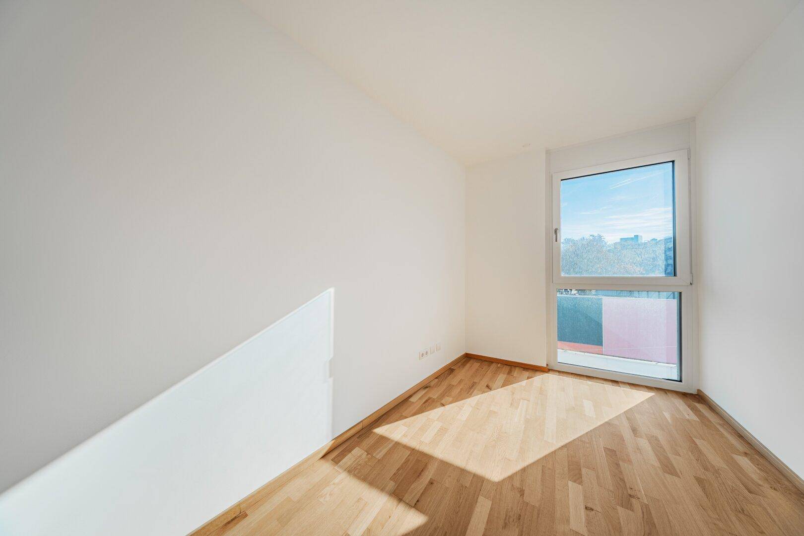 Freundlicher, leerer Raum mit Holzboden und viel Tageslicht.