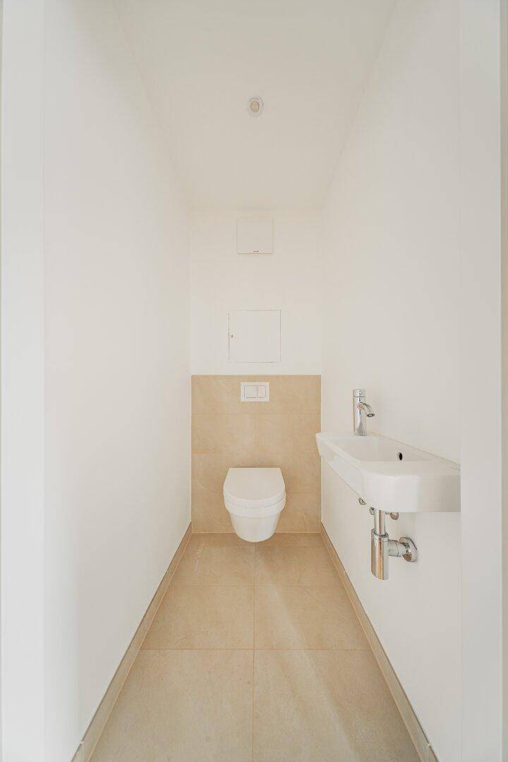 Modernes Gäste-WC mit beigefarbenen Fliesen, wandhängendem WC und kleinem Handwaschbecken.