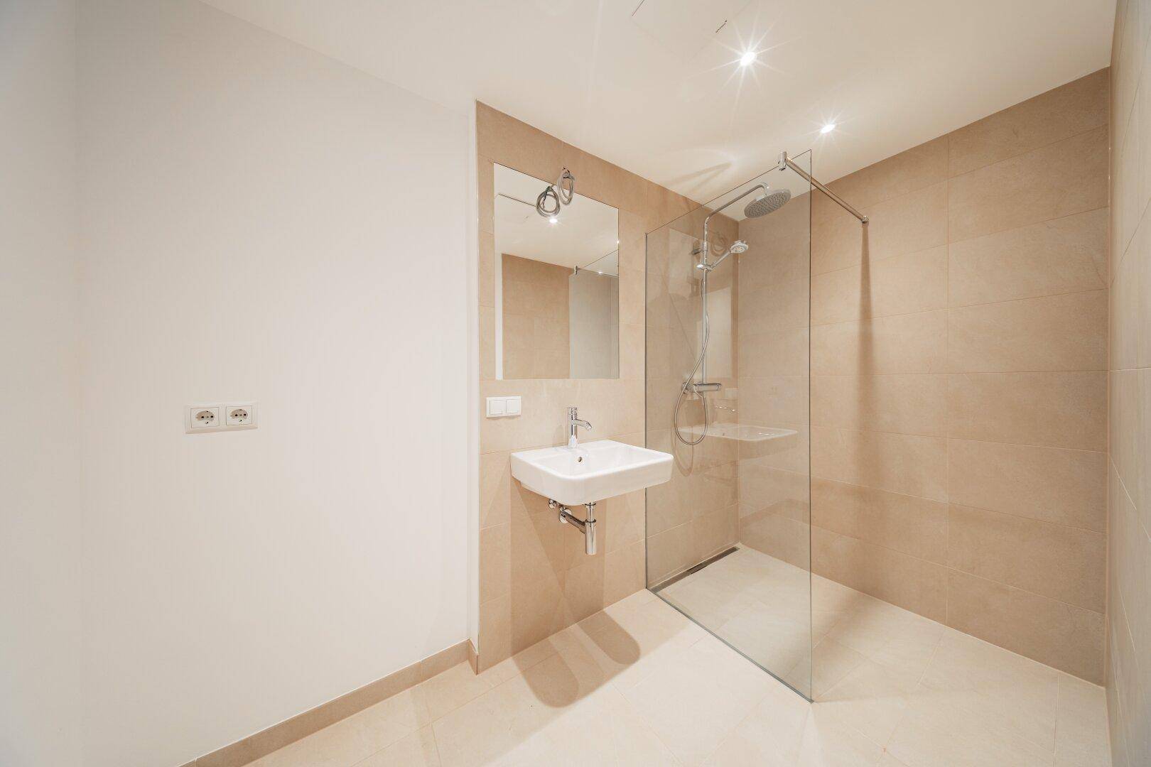 Helles, modernes Badezimmer mit beigefarbenen Fliesen, großer Dusche und minimalistischem Design.
