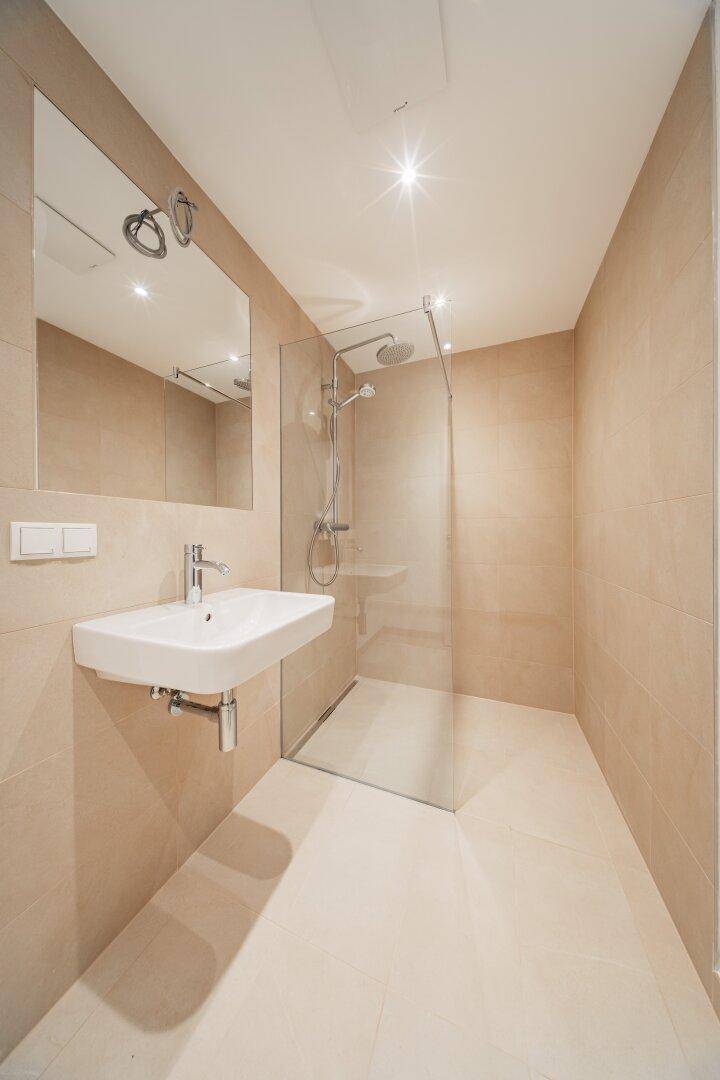 Modernes Badezimmer mit beigefarbenen Fliesen, bodengleicher Dusche und elegantem Waschtisch.