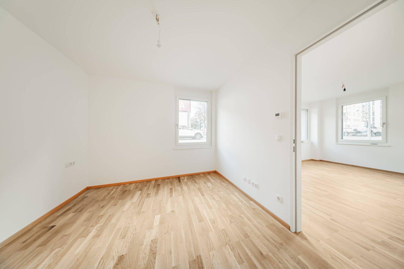 Heller Raum mit Parkettboden und Fenster, offen zu einem weiteren Zimmer, ideal für flexible Nutzung.