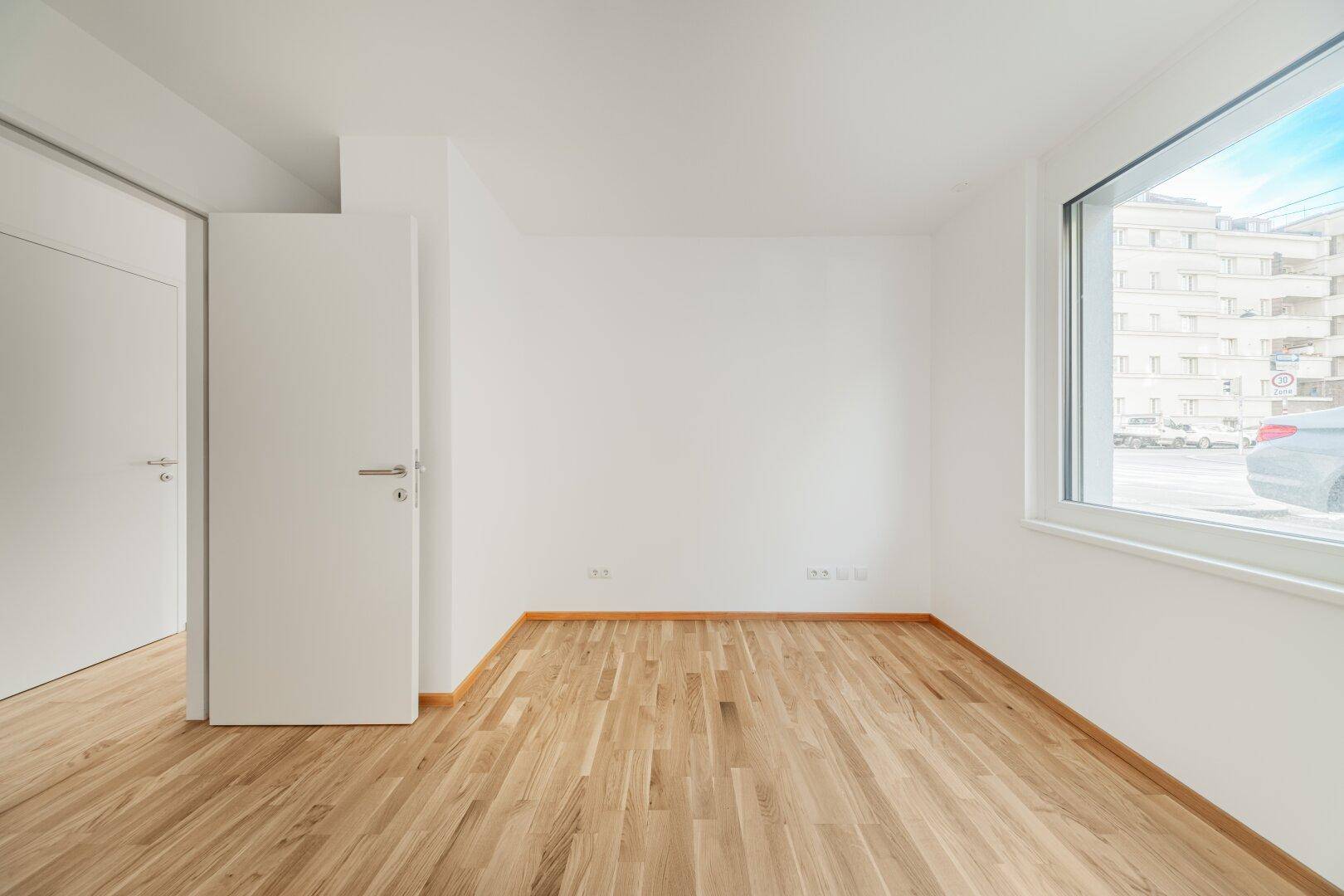 Heller Raum mit Parkettboden und großem Fenster, bietet viel Tageslicht und eine angenehme Atmosphäre.