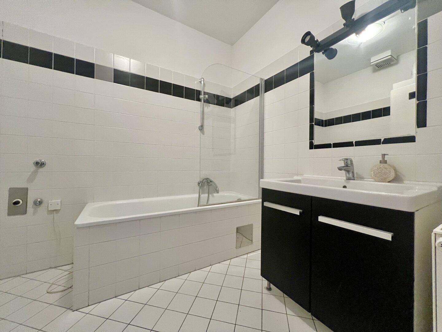 Badezimmer mit Badewanne, Duschabtrennung, Einzelwaschbecken und schwarz-weißen Fliesen.