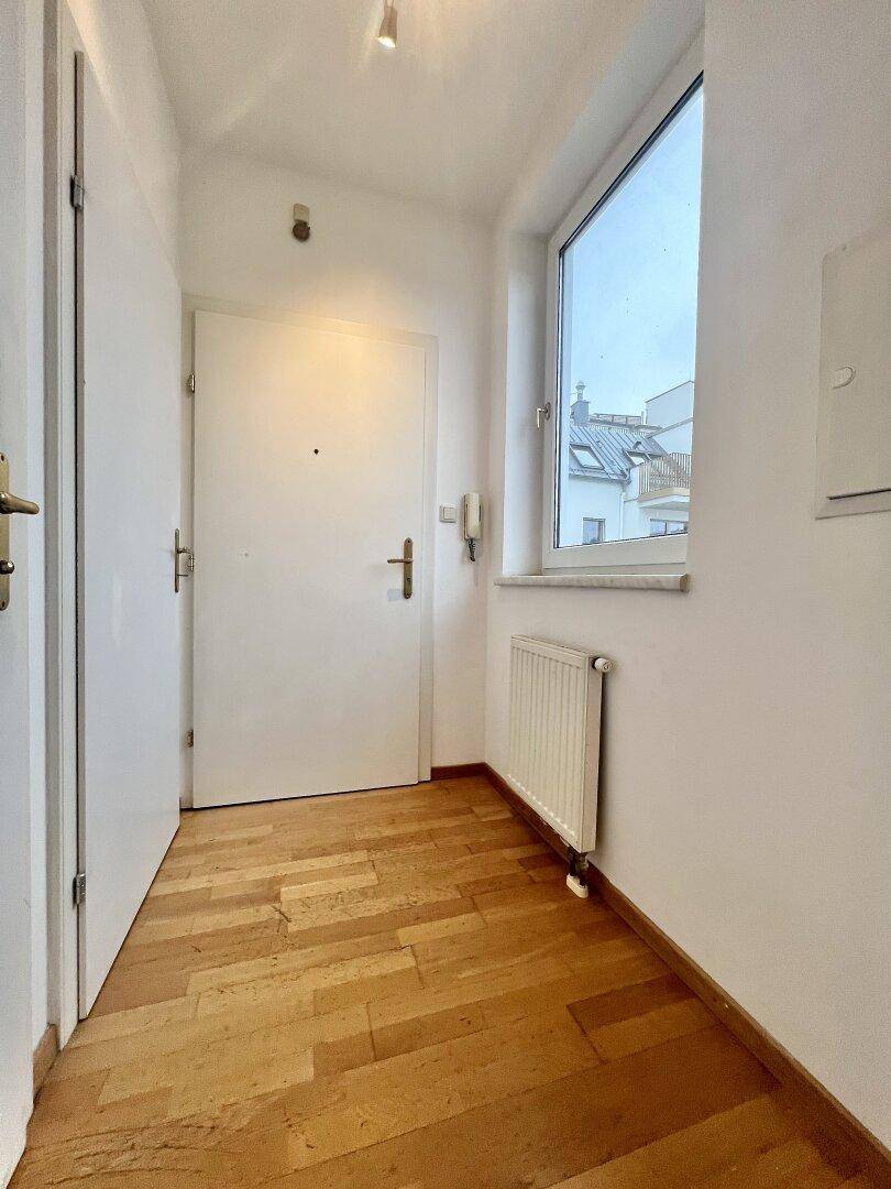 Heller Eingangsbereich mit Holzfußboden, weißer Tür und einem Fenster für Tageslicht.