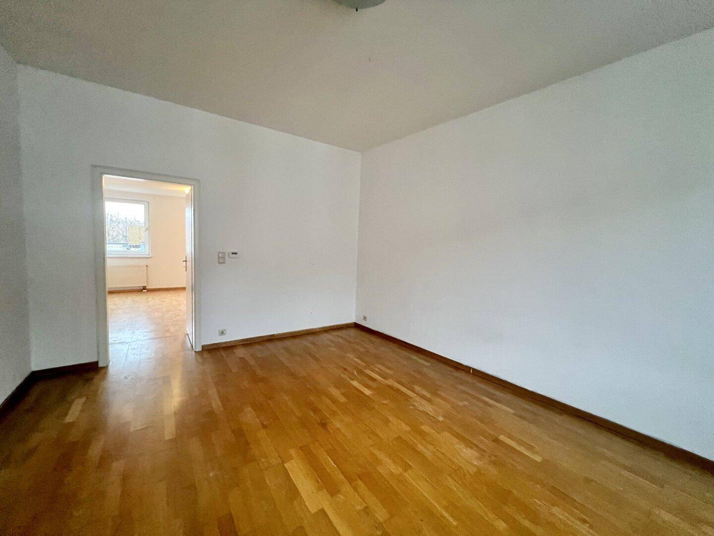 Geräumiges, helles Zimmer mit Holzparkettboden und Zugang zu einem weiteren Raum.