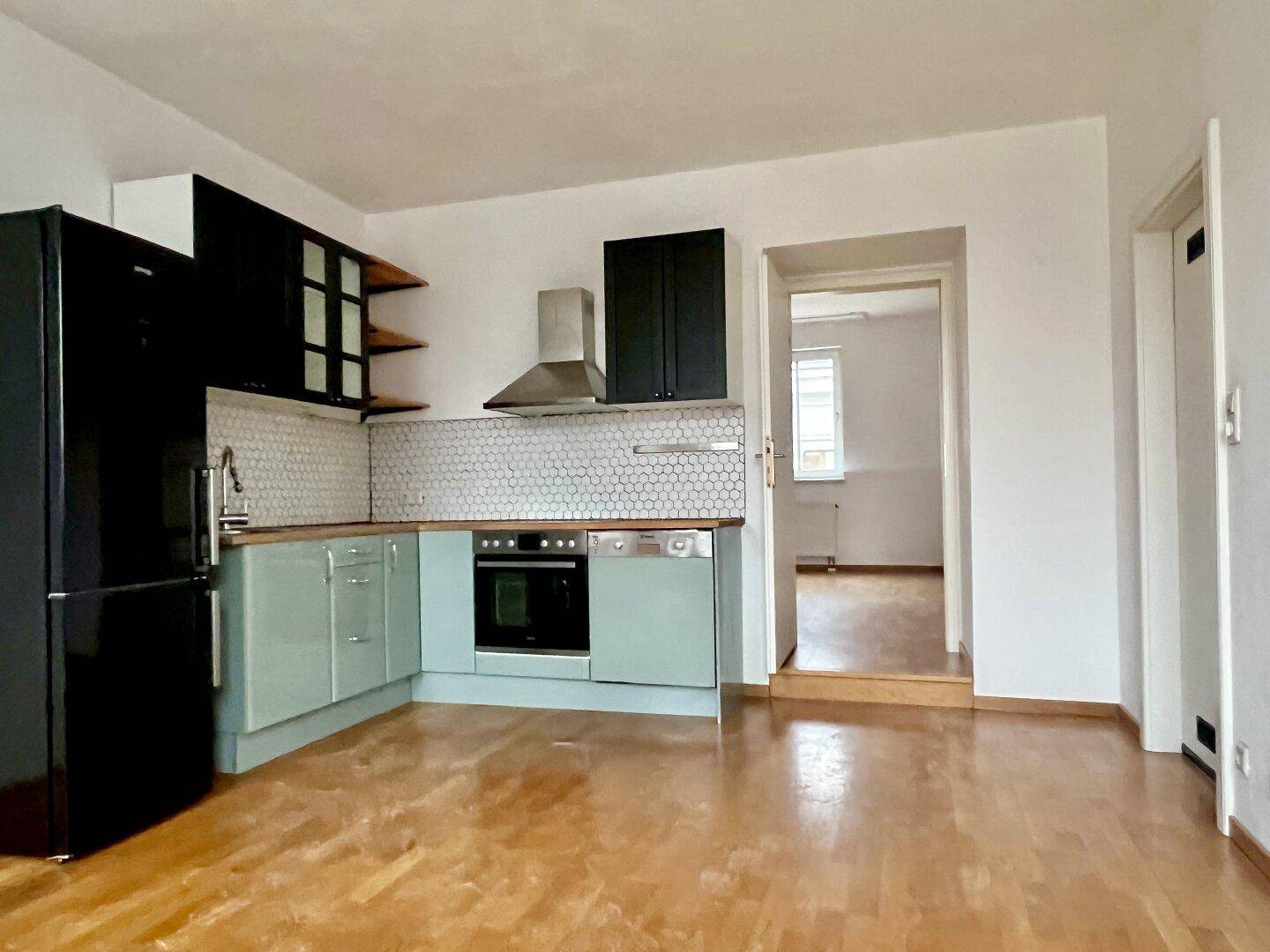 Gut ausgestattete Küchenzeile mit Kühlschrank, Backofen und Dunstabzugshaube, angrenzend an einen weiteren Raum.