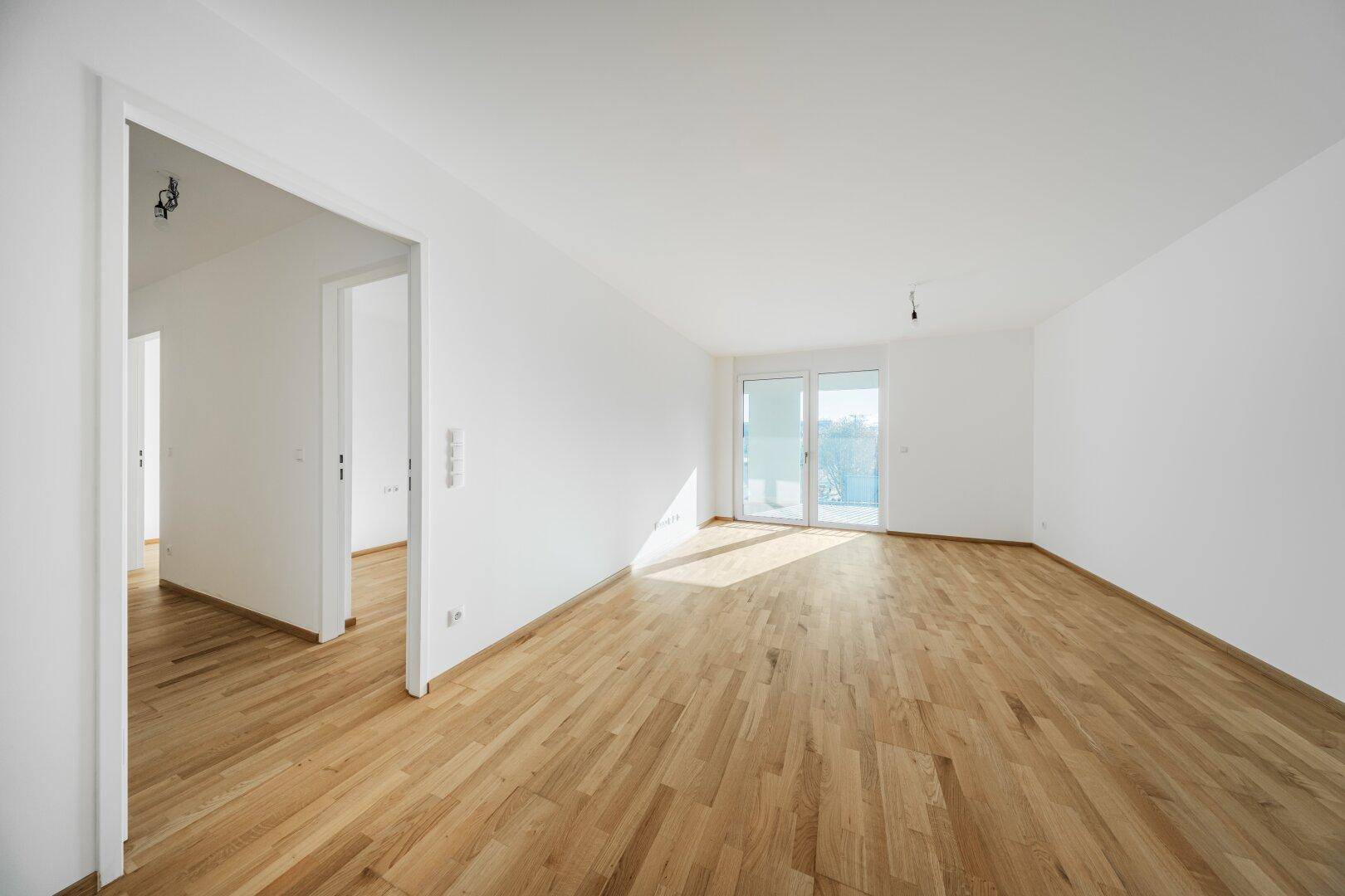 Heller, leerer Raum mit Parkettboden und Zugang zu einem Balkon.