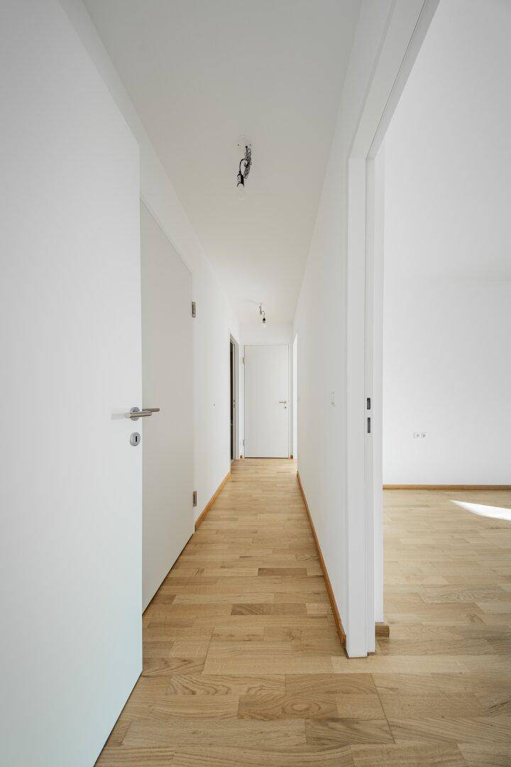 Heller Flur mit Holzboden und weißen Türen, der zu weiteren Räumen führt.