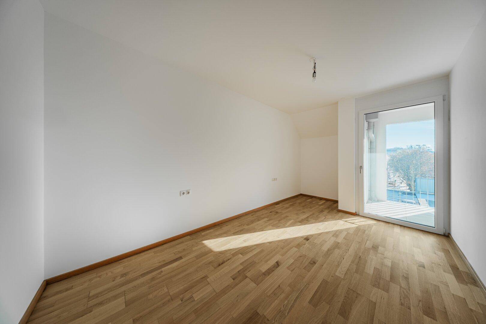Heller, unmöblierter Raum mit Parkettboden und Zugang zu einem Balkon.
