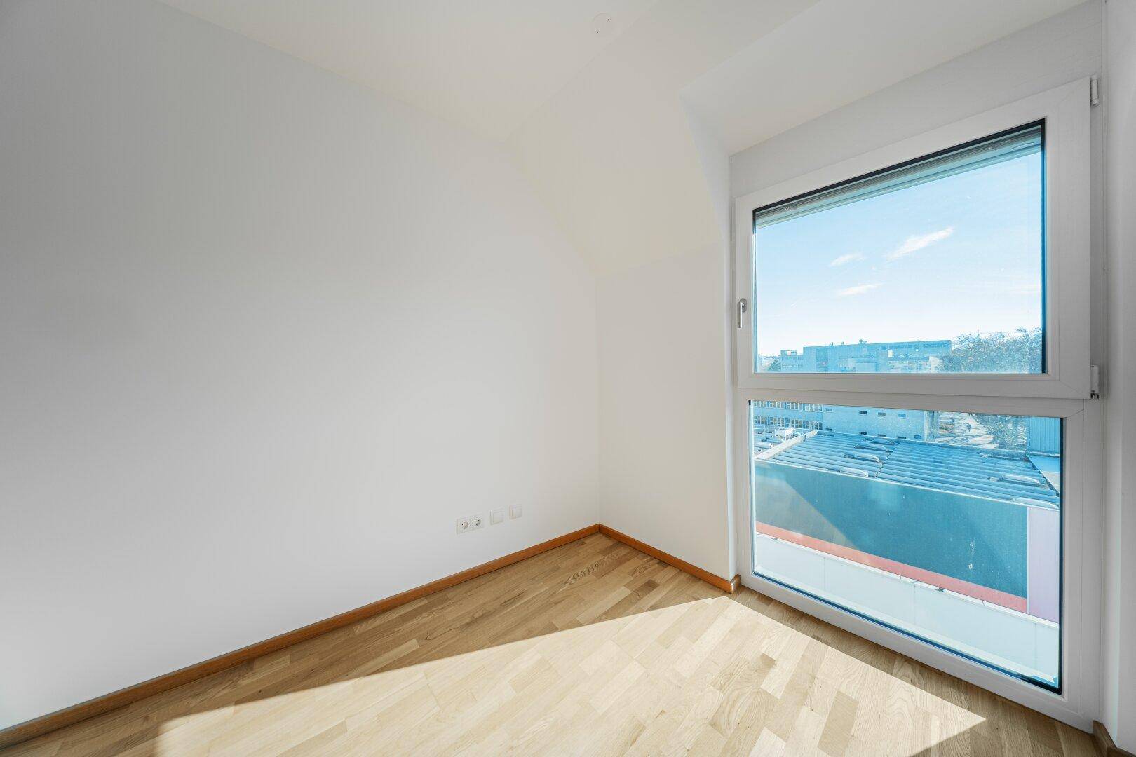 Kleiner, heller Raum mit Parkettboden und einem großen Fenster.
