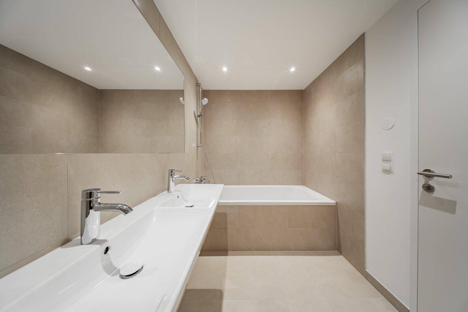 Elegantes Badezimmer mit Doppelwaschbecken, Badewanne und großem Spiegel.