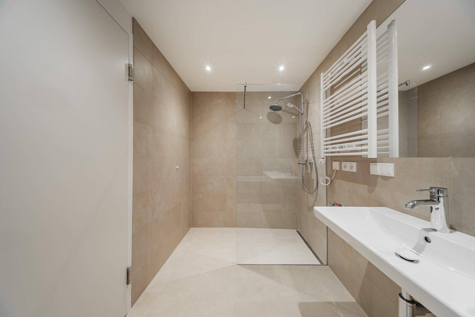 Geräumiges Badezimmer mit begehbarer Dusche, Waschbecken und beheiztem Handtuchhalter.