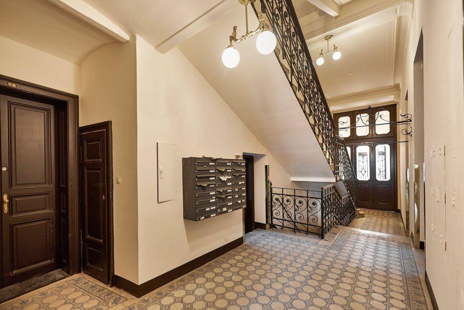 Historisches Treppenhaus mit kunstvollem Geländer und gemusterten Fliesen im Eingangsbereich.