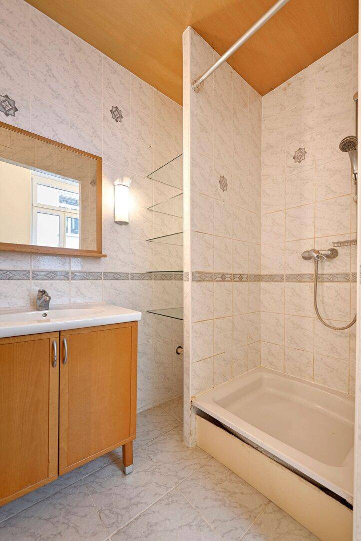 Badezimmer mit Duschkabine, Waschbeckenunterschrank und Wandfliesen im 80er-Jahre-Stil.