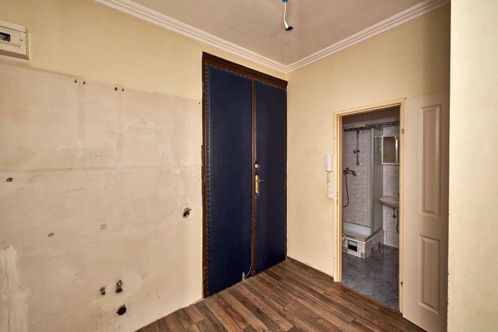 Flur mit Holzboden und Zugang zu einem Badezimmer, renovierungsbedürftiger Zustand.
