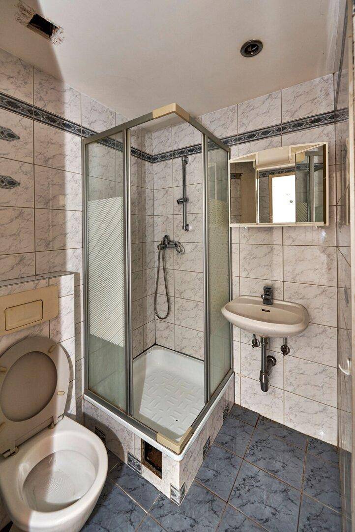 Kleines Badezimmer mit Duschkabine, WC und Waschbecken, geflieste Wände und Böden.