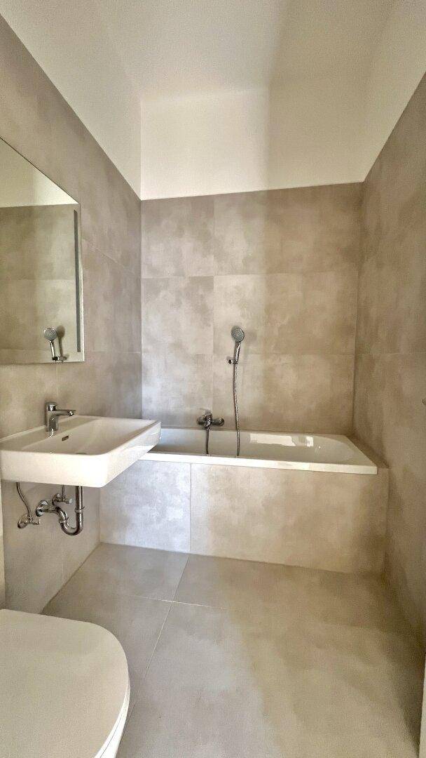 Modernes Badezimmer mit beigefarbenen Fliesen, Badewanne und Waschbecken.