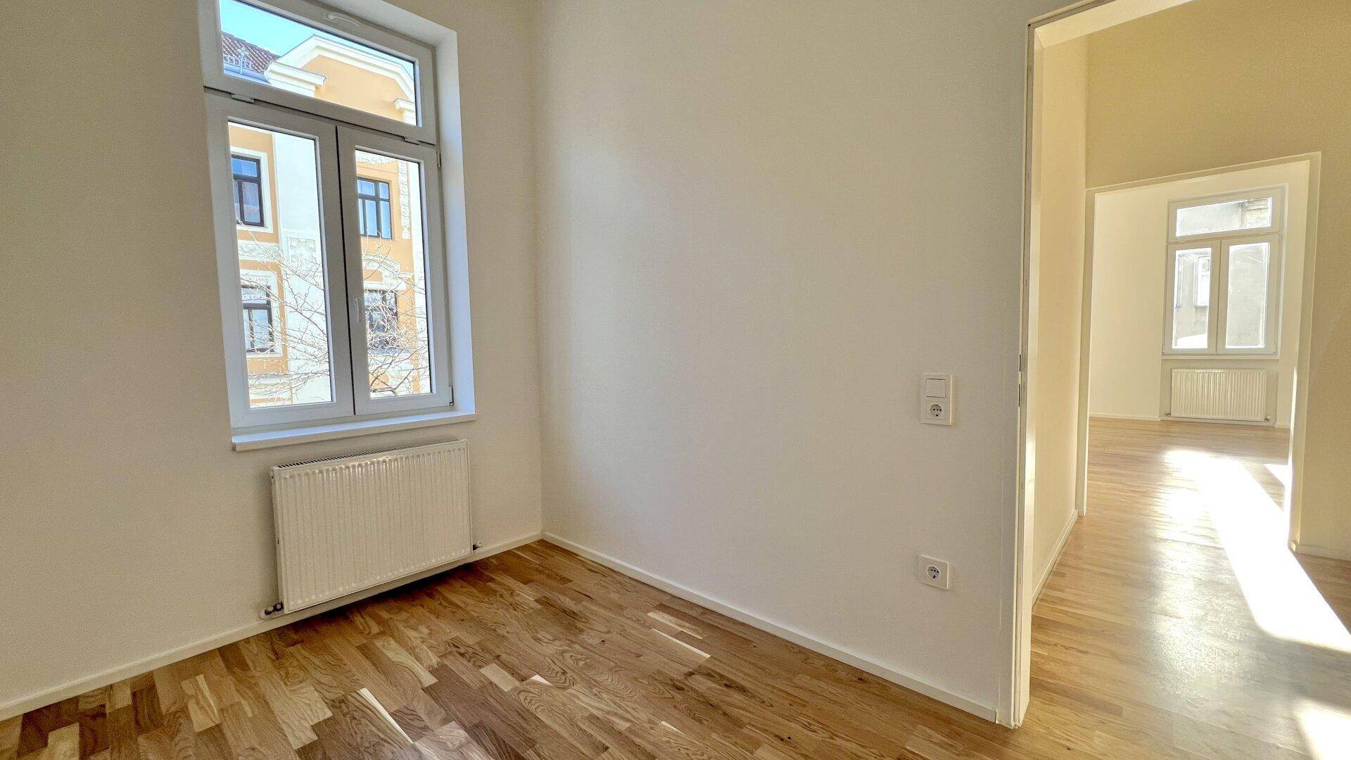 Helles Zimmer mit Parkettboden und einem Fenster, das viel Tageslicht hereinlässt.