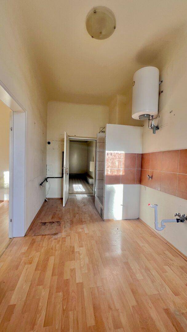 Unmöblierte Küche mit Warmwasserboiler und Anschlüssen, bereit für die Installation einer Einbauküche.
