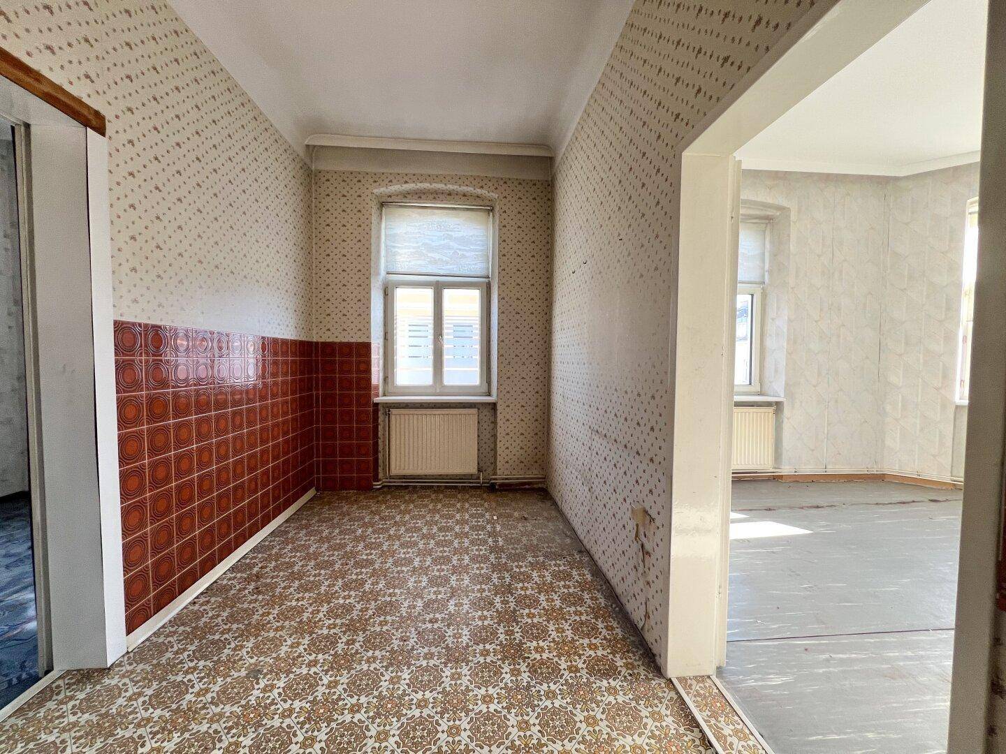 Kleiner Raum mit gemusterter Tapete, roten Fliesen und Fenster, der auf eine Renovierung wartet.