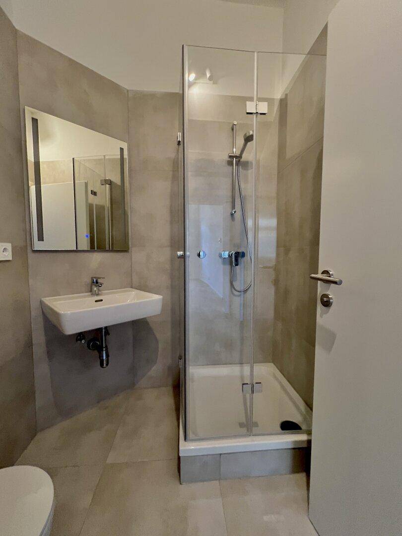 Modernes Badezimmer mit begehbarer Dusche, eleganten Fliesen und einem beleuchteten Spiegelschrank.