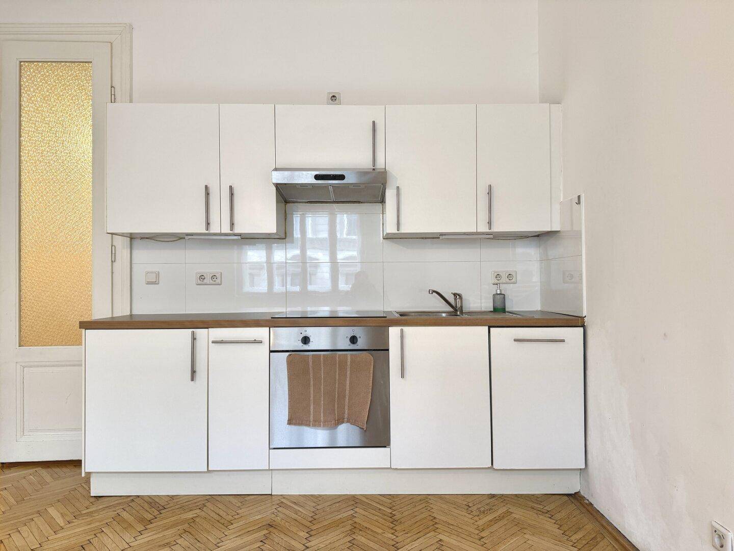 Kompakte Küche mit weißen Schränken, Holzarbeitsplatte, integriertem Backofen und Dunstabzugshaube.