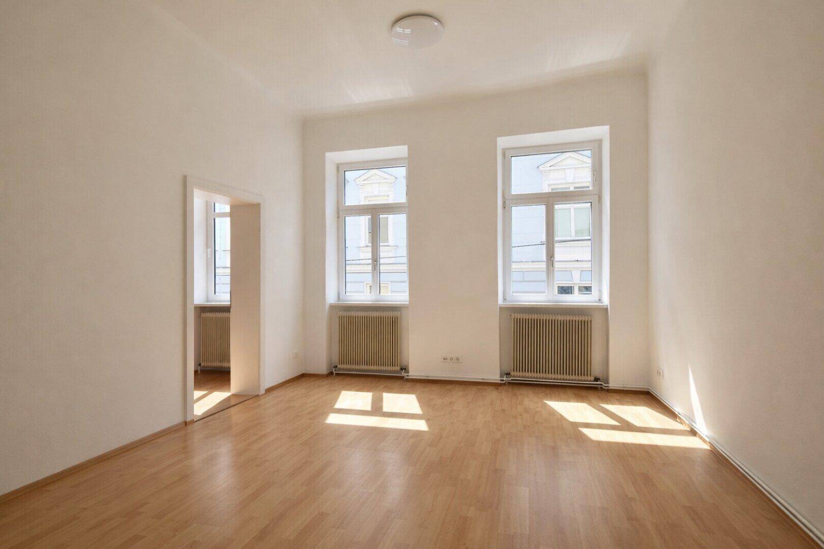 Lichtdurchfluteter Raum mit Parkettboden und Blick auf die Stadt, bereit zur individuellen Gestaltung.