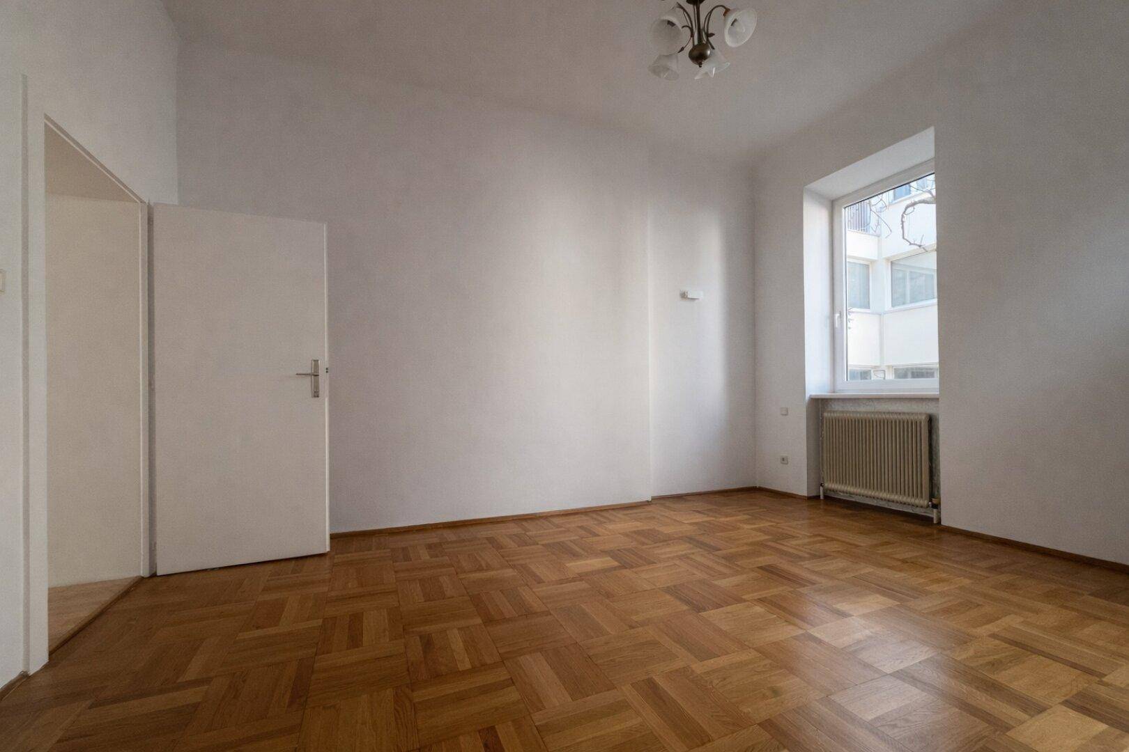 Gemütliches Zimmer mit klassischem Fischgrätparkett und Fenster, gut belichtet.