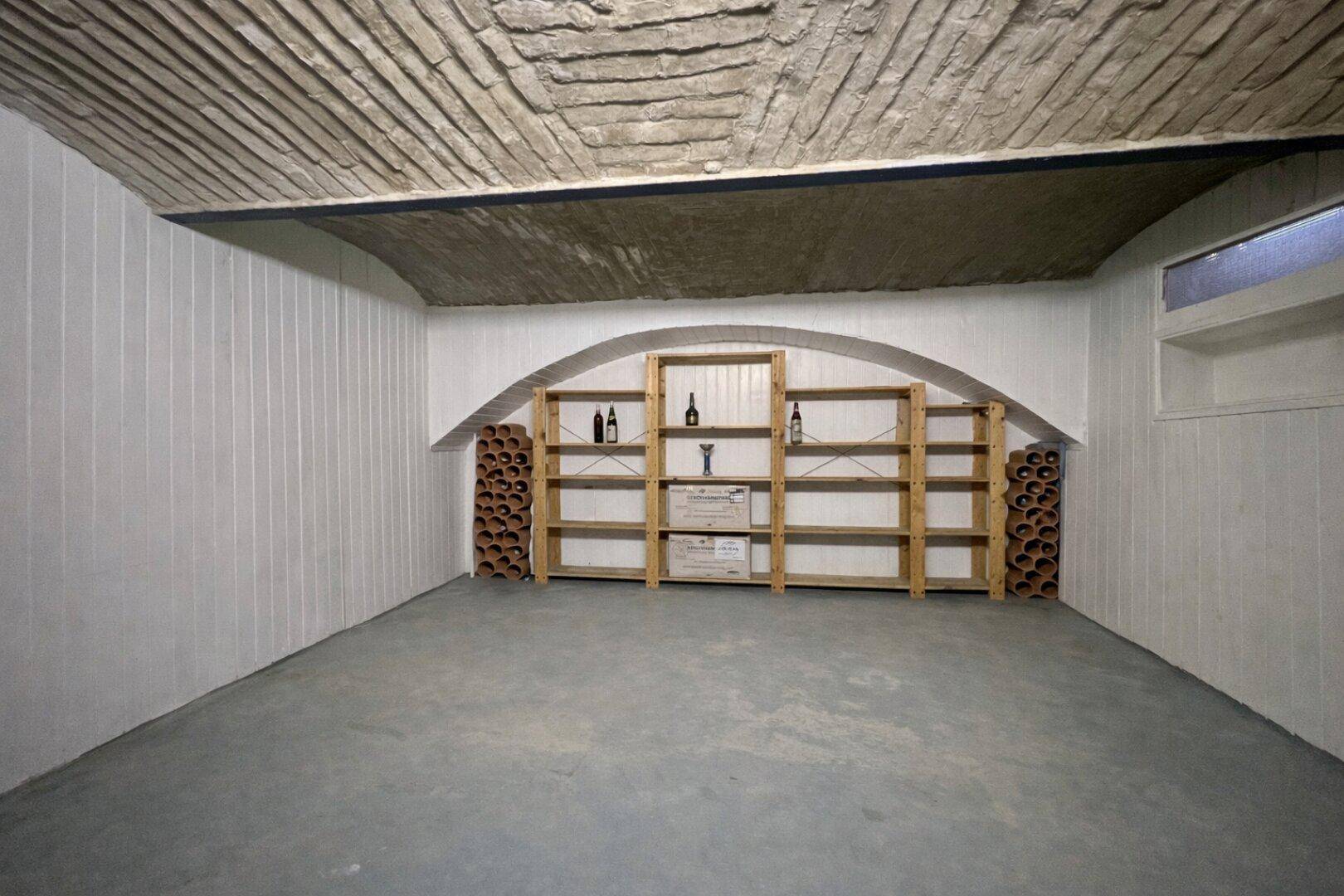 Rustikaler Weinkeller mit Steinbogen und Holzregalen, ideal zur Lagerung von Weinflaschen.