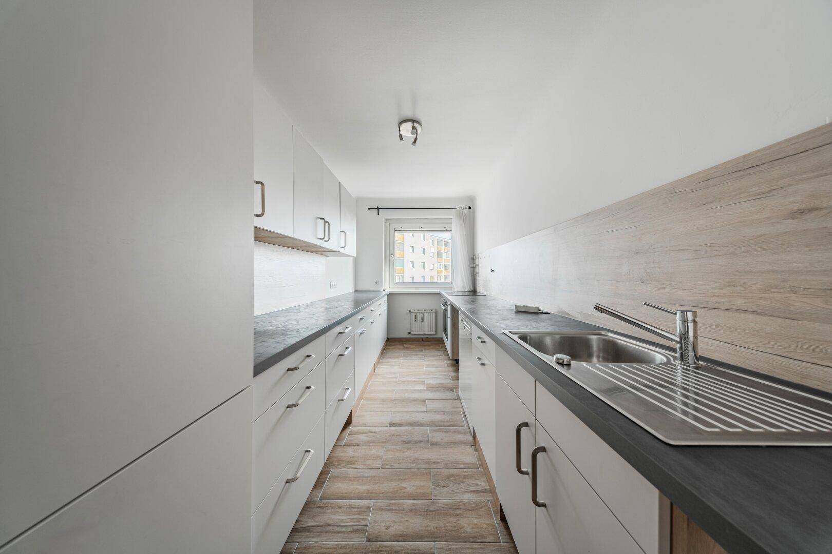 Moderne, schmale Küche mit weißen Schränken, dunkler Arbeitsplatte und Holzboden.