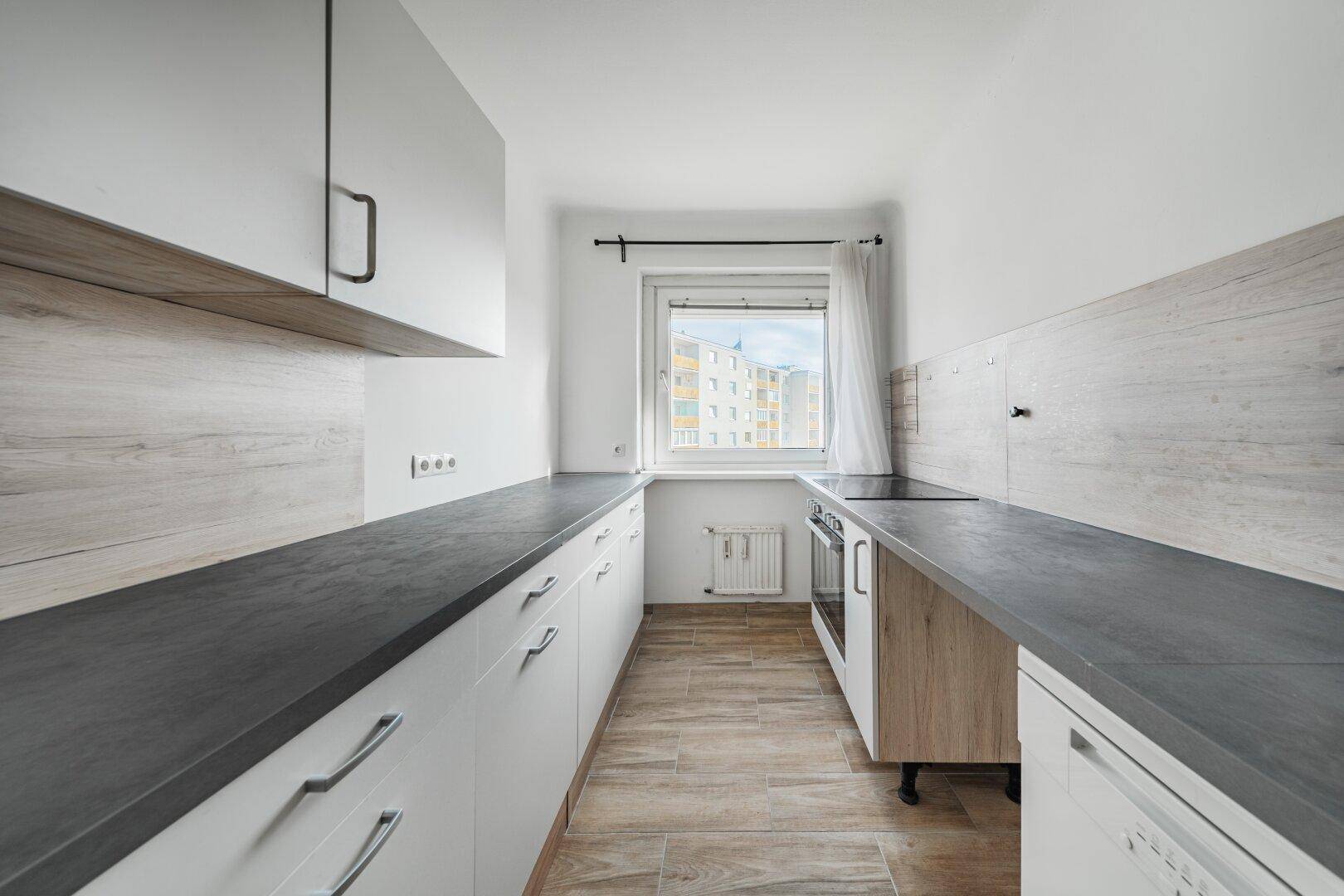 Helle Einbauküche mit weißen Fronten, Holzdetails und Fenster mit Stadtblick.