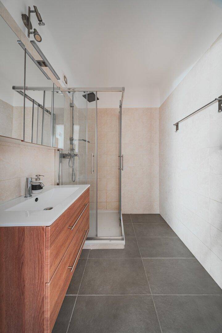 Modernes Badezimmer mit Duschkabine, Holzwaschtisch und hellen Fliesen.