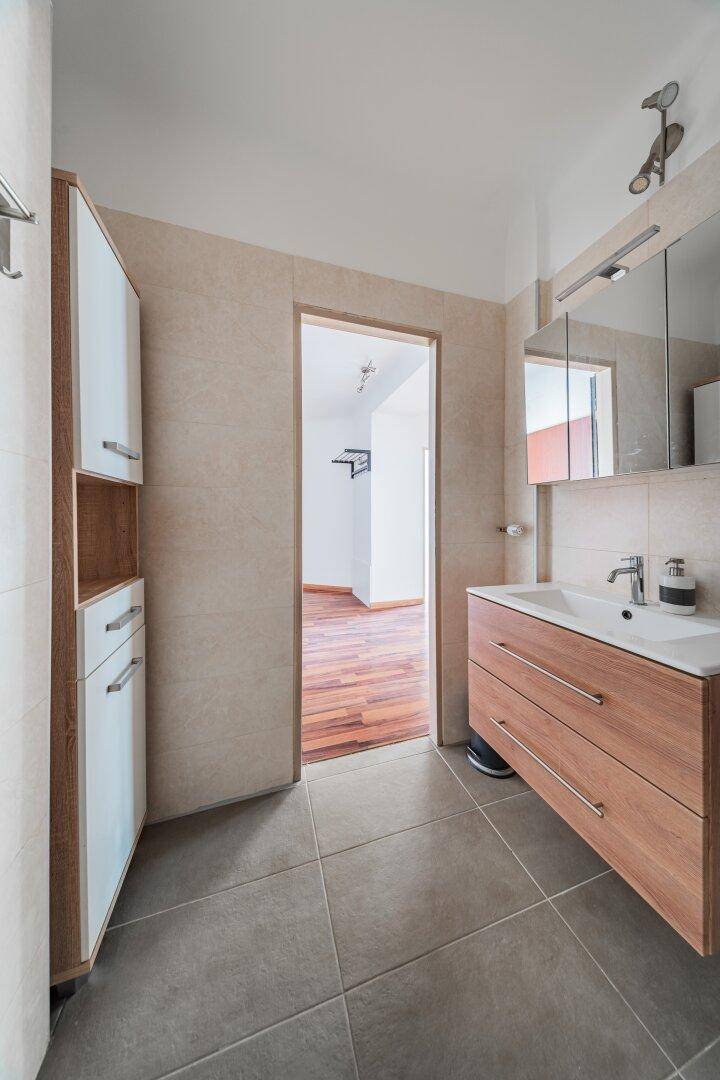 Helles Badezimmer mit Waschtisch, Spiegelschrank und Zugang zum Flur.