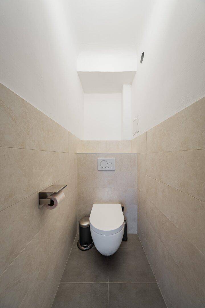 Separates WC mit Wand-WC und hellen Fliesen in modernem Design.