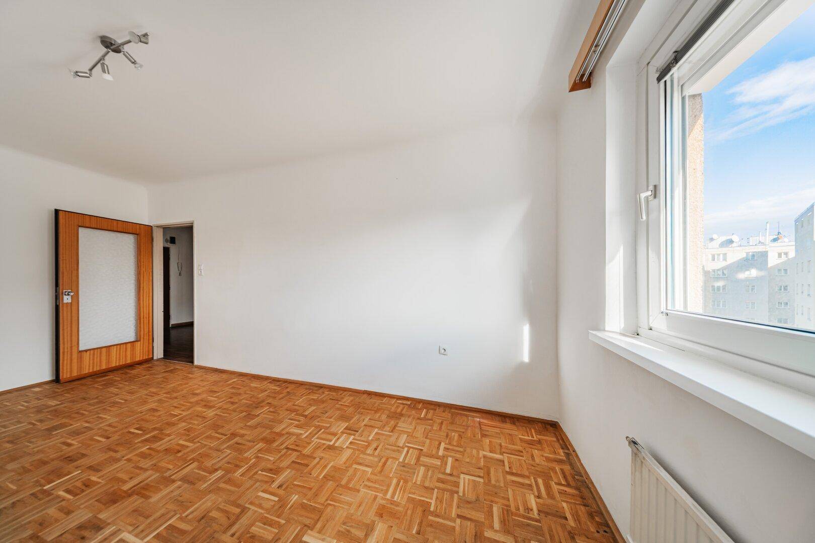 Helles Schlafzimmer mit Parkettboden und Fenster mit Blick auf die Umgebung.