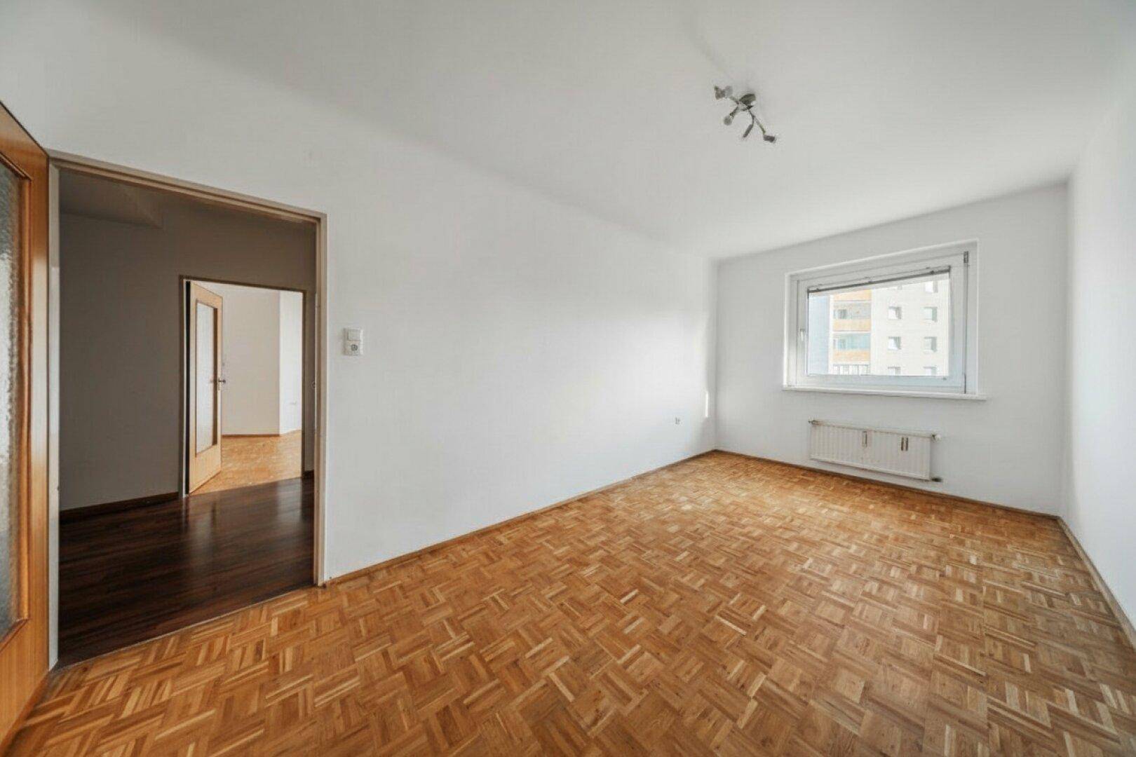 Unmöbliertes Schlafzimmer mit Parkettboden und Zugang zu einem weiteren Raum.