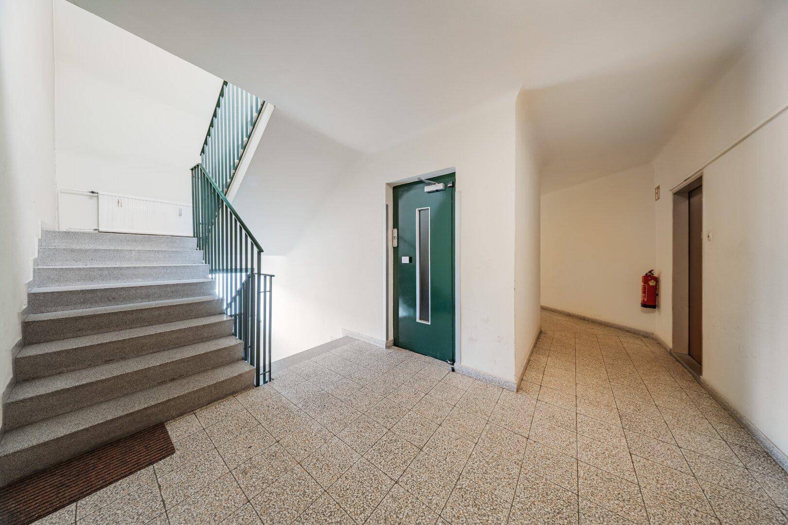 Gemeinschaftlicher Treppenhausbereich mit Aufzug und Fliesenboden im Gebäude.