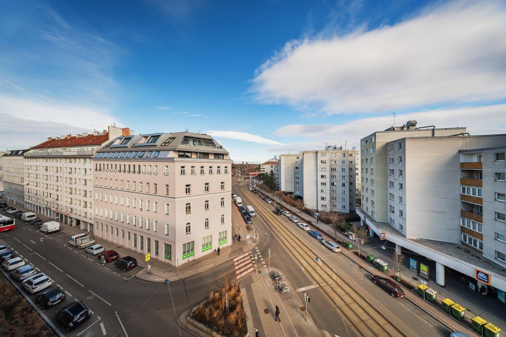 Stadtansicht mit Straßenbahnlinien, umliegenden Gebäuden und blauem Himmel.