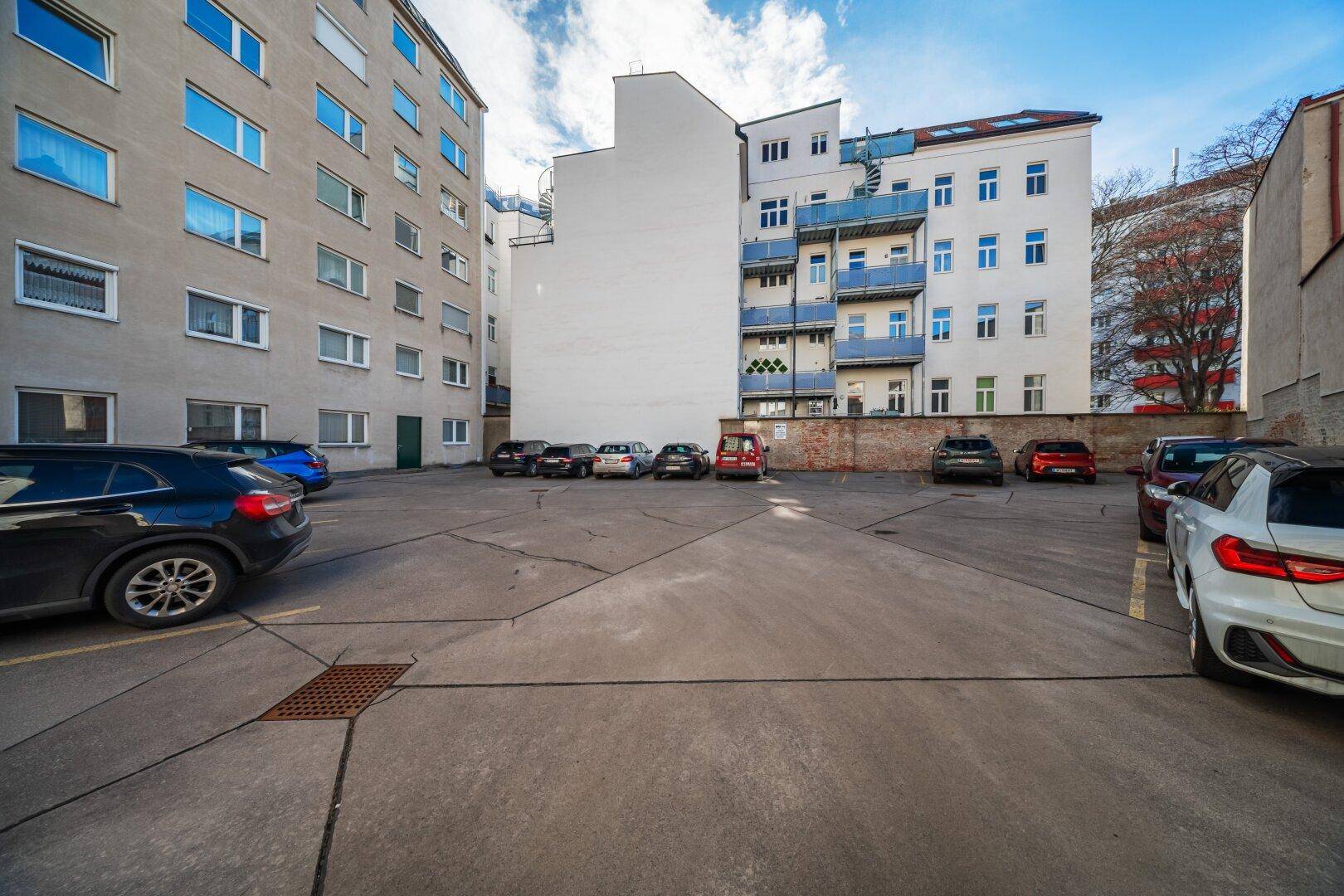 Außenparkplatz mit mehreren abgestellten Fahrzeugen hinter dem Gebäude.