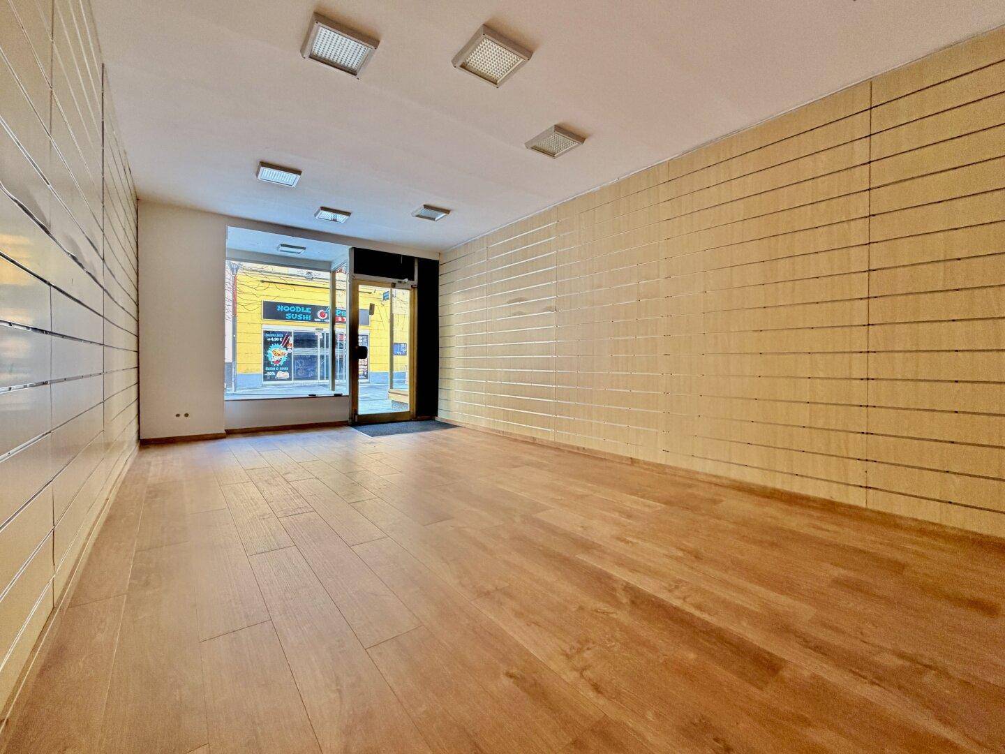Leerer Ladenraum mit Holzboden und gestreiften Wänden, bereit für neue Mieter.