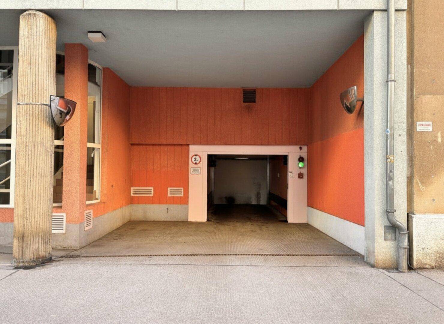 Eingang zu einer Tiefgarage mit orangefarbener Fassade und Säulen.