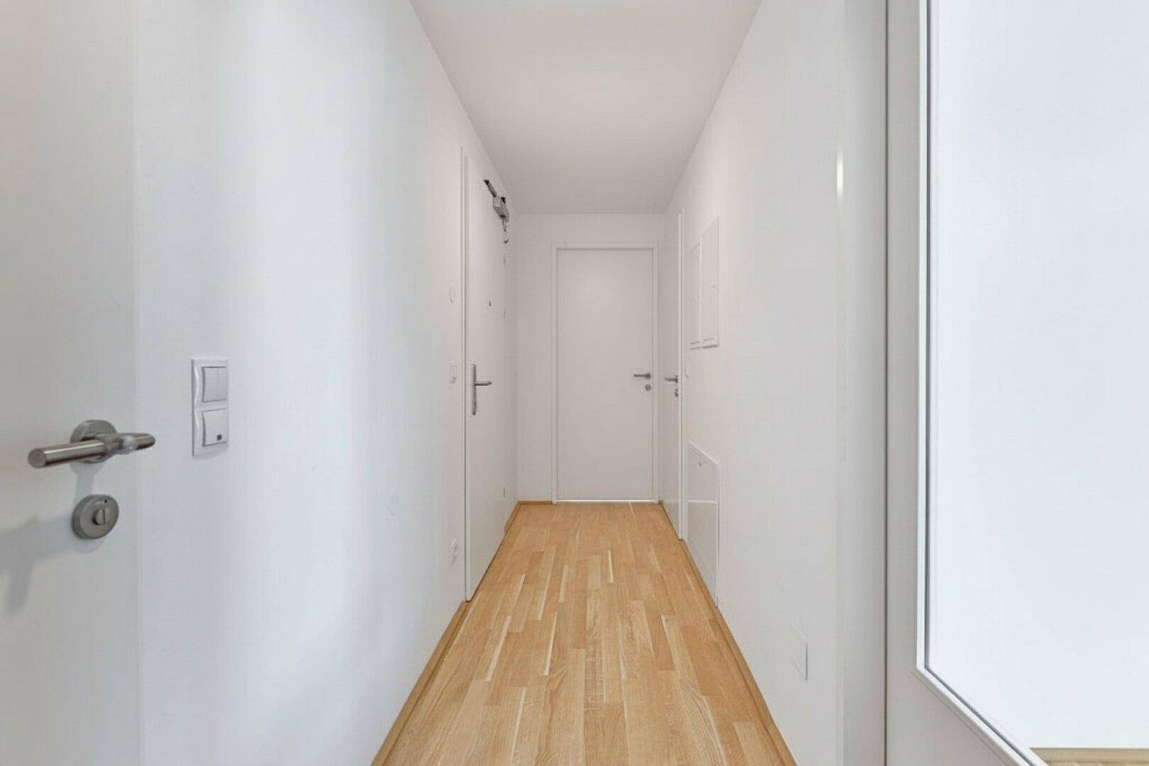 Heller Flur mit Parkettboden und weißen Wänden, verbindet die verschiedenen Räume der Wohnung auf moderne Weise.