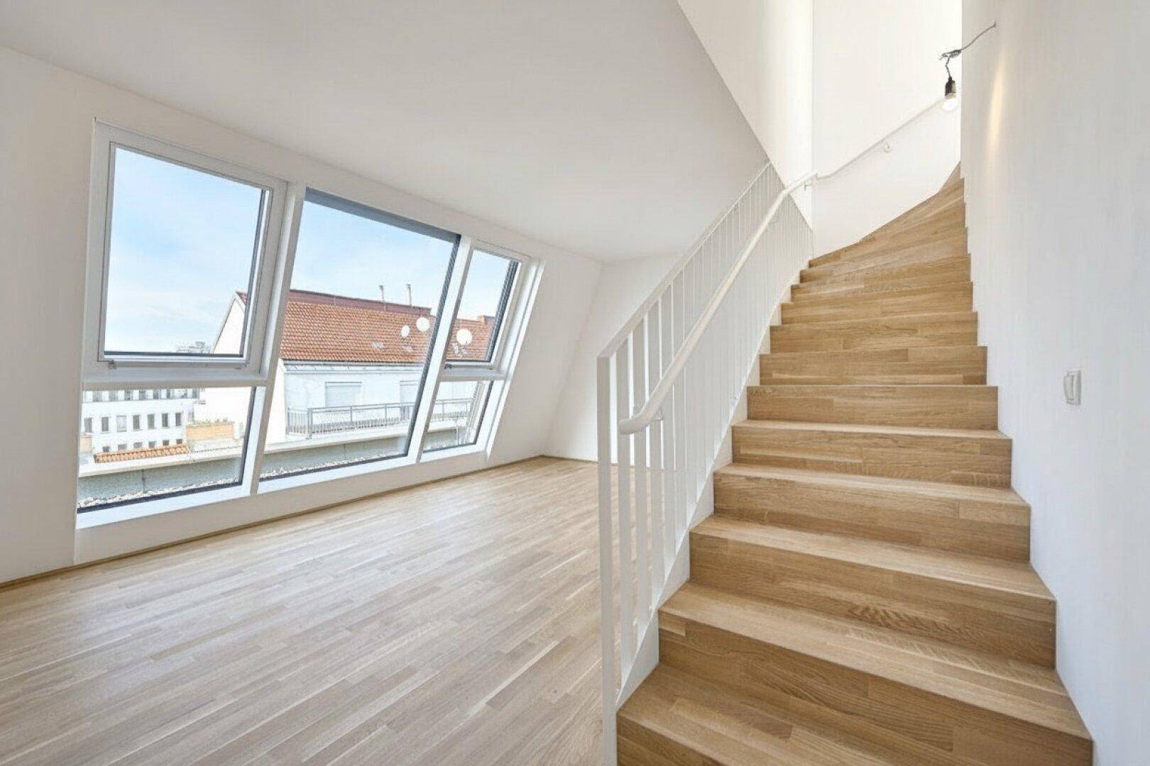 Geräumiger Raum mit Holztreppe, großen Fenstern und Parkettboden, bietet einen beeindruckenden Blick über die Stadt.