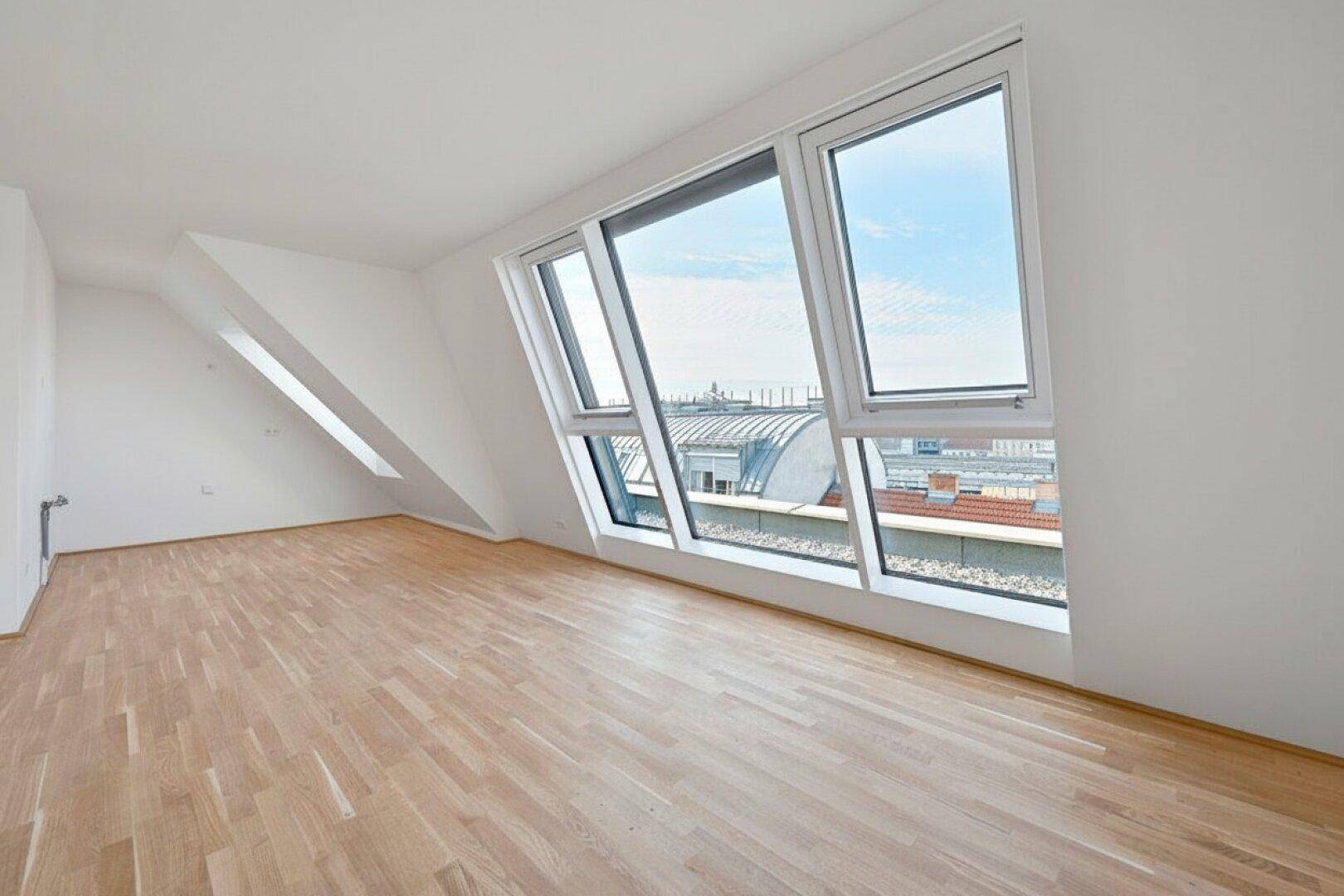 Heller Raum mit großen, schrägen Fenstern und Parkettboden, bietet einen weiten Blick über die Stadtlandschaft.