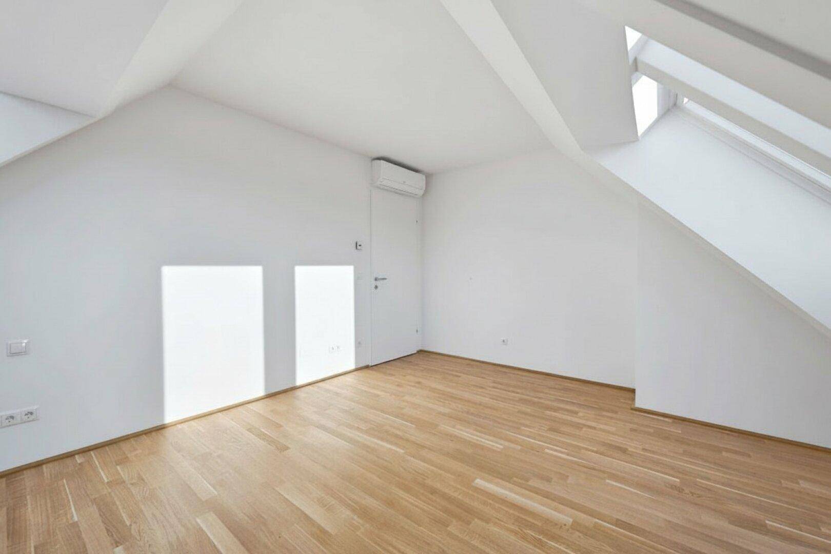 Heller Raum mit Dachschräge, Dachfenster und Klimaanlage, bietet eine angenehme Wohnatmosphäre mit viel Tageslicht.