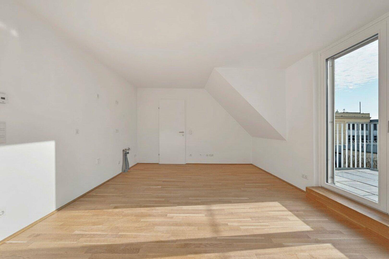 Geräumiger, leerer Raum mit Holzboden und großem Fenster mit Zugang zu einer Terrasse.