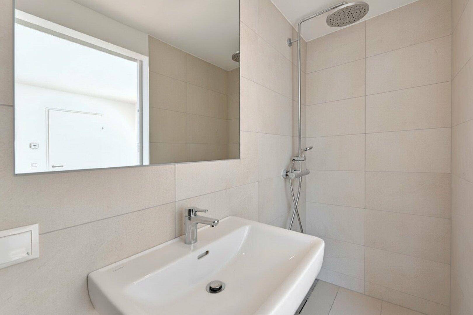 Modernes Badezimmer mit Duschbereich, Einzelwaschbecken und hellen Fliesen an den Wänden.